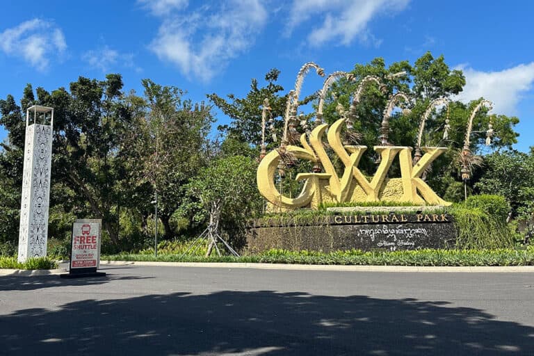 Large "GWK Cultural Park" sign surrounded by greenery under a blue sky; free shuttle sign on the left at Garuda Wisnu Kencana.