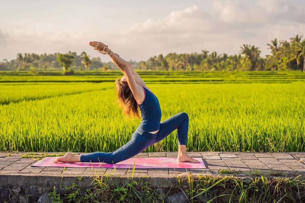 A person practicing yoga on a pink mat in a lush green field under a cloudy sky, reminiscent of serene Bali landscapes.