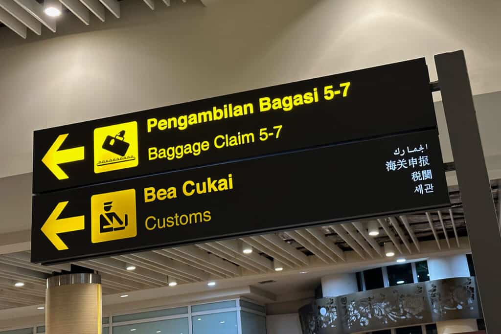 A Bali Airport Sign displays directions to Baggage Claim 5-7 and Customs in multiple languages, guiding travelers with clear and vibrant instructions.