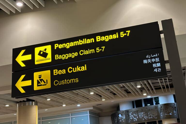 A Bali Airport Sign displays directions to Baggage Claim 5-7 and Customs in multiple languages, guiding travelers with clear and vibrant instructions.
