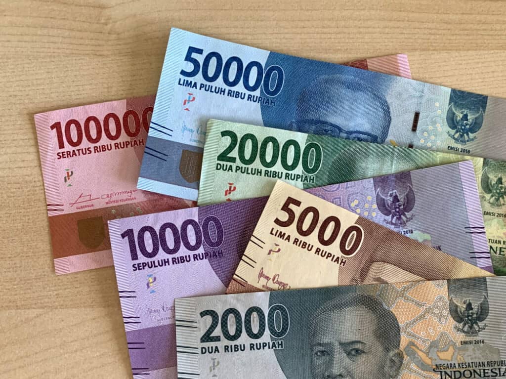 Six Indonesian rupiah banknotes of different colors and denominations arranged on a wooden surface.