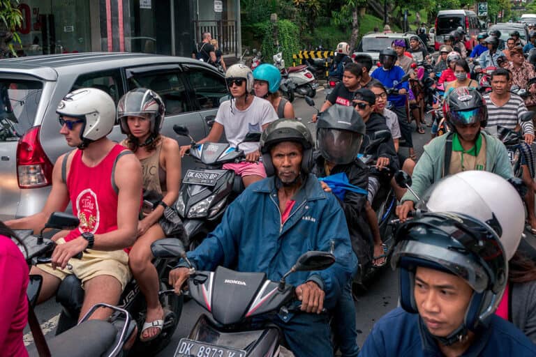 Crowd of people riding motorcycles and scooters in heavy Bali traffic.